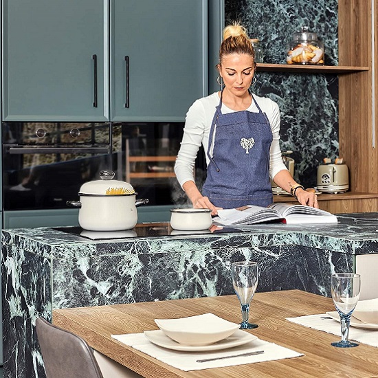 una mujer leyendo en un libro en una cocina revestida con encimeras Laminam Verde Alpi