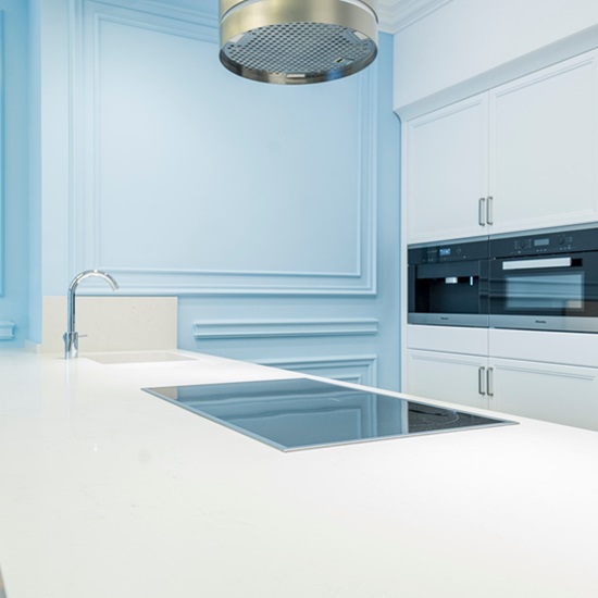 una cocina con muebles blancos y azules con una encimera de cuarzo Blanco Puro Levantina Quartz