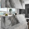 Cocina moderna con isla Arklam Invisible Grey gris veteada, gabinetes negros, fruta y vista oceánica.