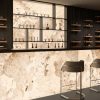 Bar moderno con revestimientos retroiluminados Arklam Patagonia Gold en Málaga, botellas y mobiliario negro.