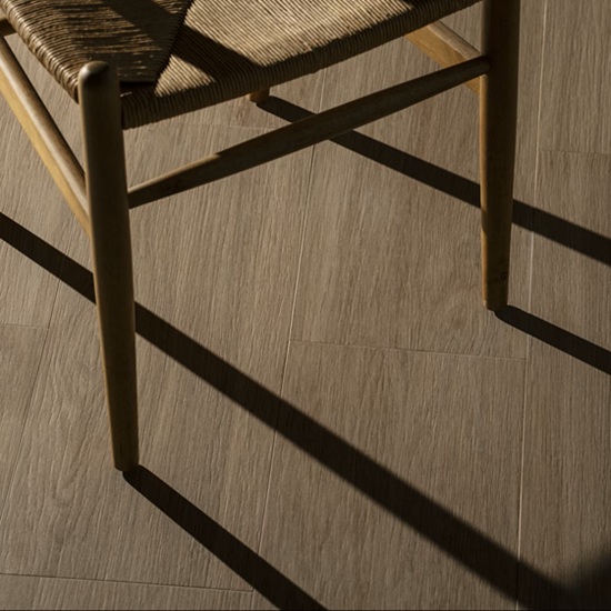 Primer plano de pierna de silla sobre suelo Dekton Kedar en tono roble, con sombra y textura detallada.
