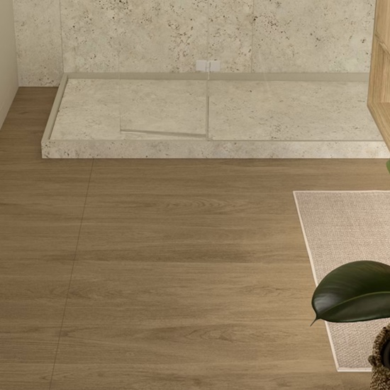 Suelo Dekton Kedar en baño con plato de ducha blanco, alfombra y planta, en tono roble cálido.