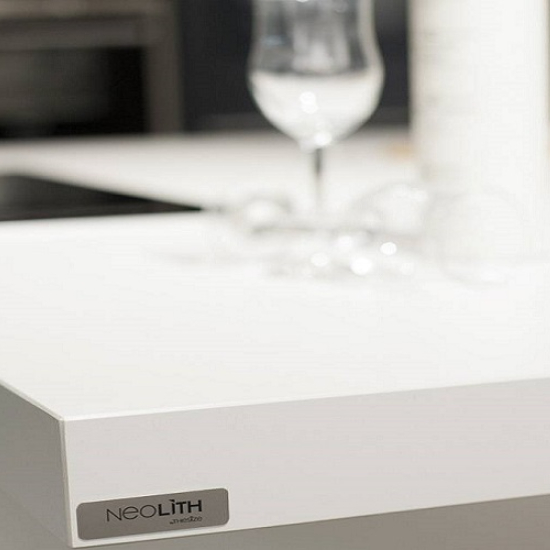 Primer plano de encimera blanca Neolith Arctic White con vaso y etiqueta de marca.