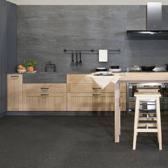 Cocina con encimera Neolith Aspen Grey gris, gabinetes madera, fregadero y taburete en suelo negro.