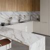 Cocina con encimera Neolith Azure blanca, gabinetes blancos, grifo negro y electrodomésticos integrados.