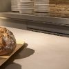 Encimera Neolith Barro terracota con pan fresco sobre tabla de cortar en cocina con estantes.