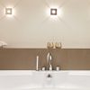 Bañera blanca con revestimiento Neolith Barro terracota, grifo plateado y velas doradas en baño minimalista.
