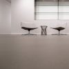 Sala minimalista con sillas blancas y mesa plateada sobre suelo Neolith Barro terracota.