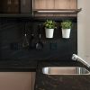 Salpicadero y encimera Neolith Mamba Málaga, superficie negra dorada con utensilios y vegetación.