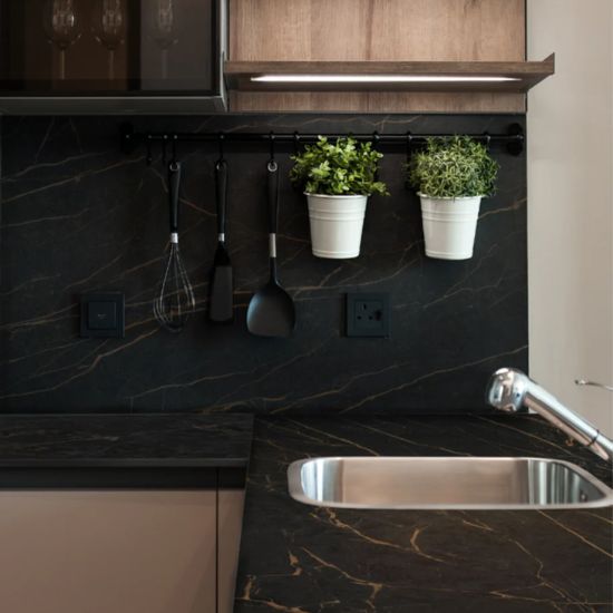 Salpicadero y encimera Neolith Mamba Málaga, superficie negra dorada con utensilios y vegetación.
