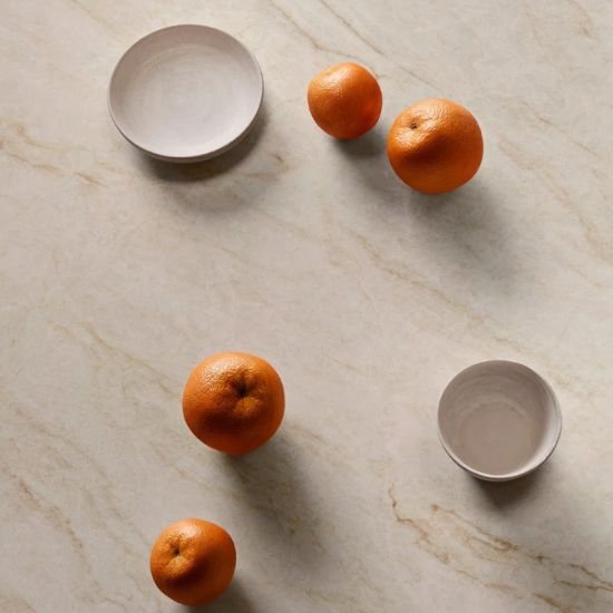 Superficie Neolith Taj Mahal Málaga con frutas y vajilla, textura beige luminosa resistente.