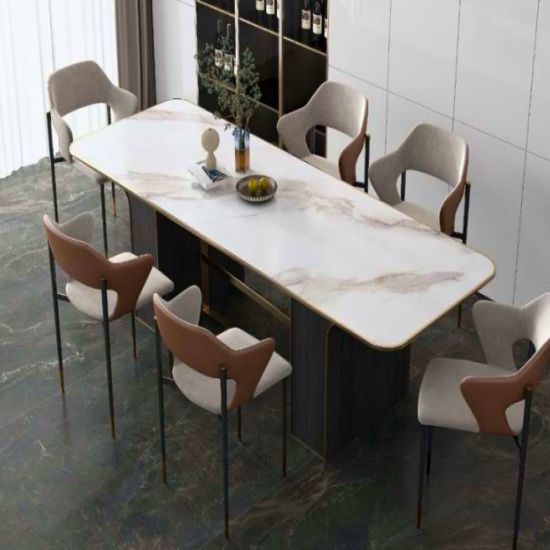 Mesa de comedor Blaker Statuario Gold blanca veteada con sillas beige, fruta y gabinetes oscuros en sala luminosa.