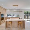 Cocina con isla Blaker Statuario Gold blanca veteada, taburetes de madera, luz lineal y gabinetes blancos en ambiente espacioso.