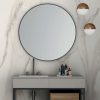 Vanitorio Blaker Toscana Gold blanca veteada con espejo redondo, grifo negro y productos en baño elegante.