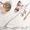 Encimera Blaker Statuario Bernini blanca veteada con sartén en fuego, verduras y utensilios en cocina moderna.