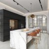 Cocina moderna con isla Blaker Statuario Bernini blanca veteada, pan, sillas naranjas y gabinetes oscuros en ambiente elegante.