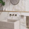 Baño moderno con vanitorio Blaker Venatino Gold blanca veteada, espejo redondo, grifo bronce y estante en ambiente cálido.