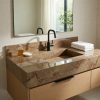 Baño moderno con encimera de baño Mármol Marrón Alhambra marrón veteado, grifo negro, toallas blancas y planta en ambiente cálido.