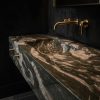Mueble de baño en Cuarcita Verde Amazona con lavabo integrado y grifería dorada sobre fondo negro