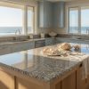 Isla de cocina en Granito Crema Julia con vistas al mar, muebles azul claro y fregaderos integrados